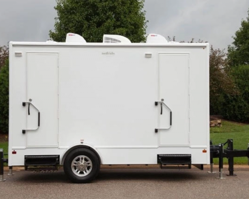a white 2 stall restroom trailer rental parked on a driveway for an event